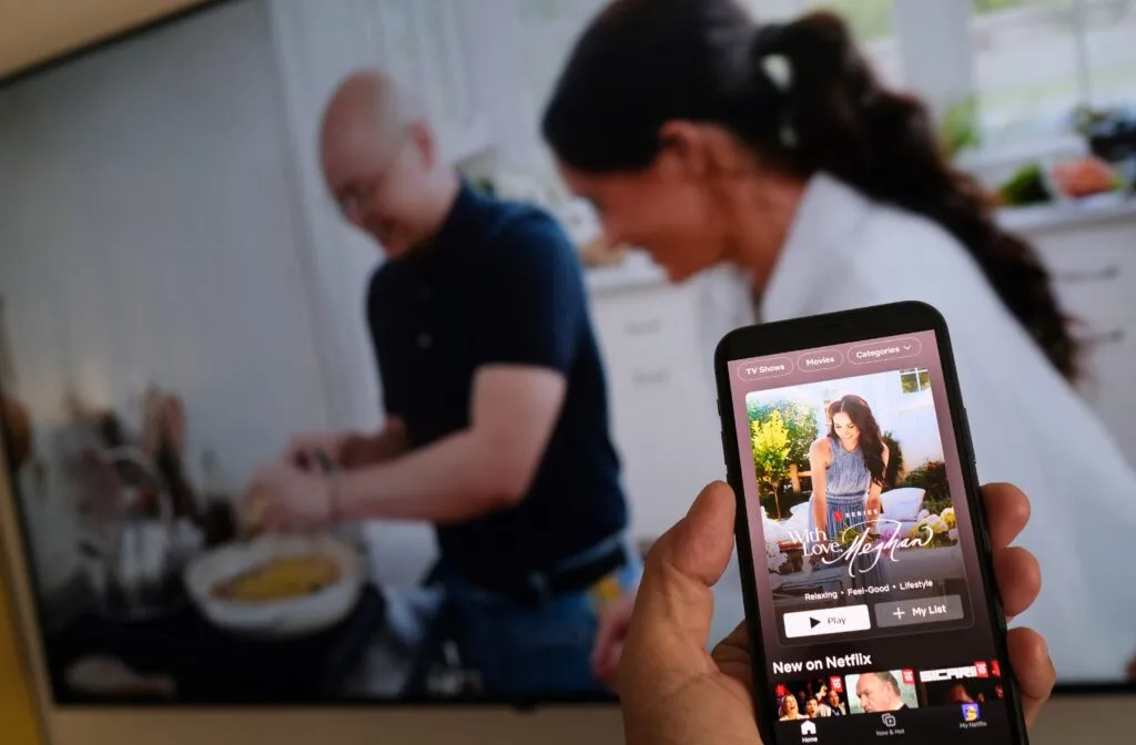 A viewer watches a clip from Meghan’s Netflix show while a TV plays scenes from the same series